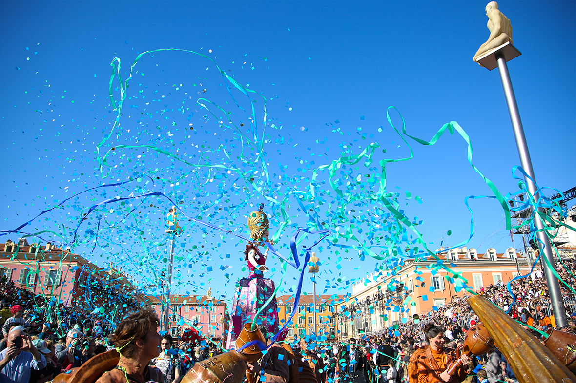 Blue confetti and ribbons shooting into the air with buildings and a crowd in the background